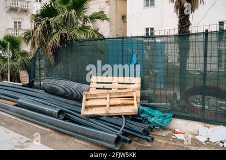 Pipes and wooden pallets lie near a house under construction on a background of green palm trees Stock Photo