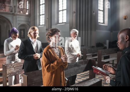 Group of people standing and listening the pray while priest reading it in the church Stock Photo