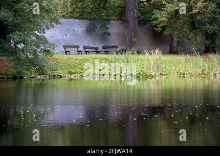 Three empty benches facing a lake in a park by a beautiful, colorful, summer sunrise. Cesky Krumlov, Czech Republic. Stock Photo