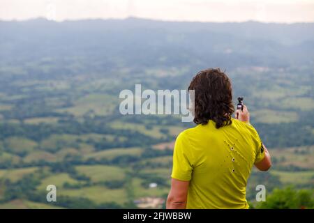 A long-haired man filming a video with a small video camera, a picturesque valley. Dominican Republic on the mountain. Stock Photo