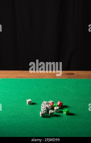 View of green baize with white, green and red dice on wooden table and black background, in vertical, with copy space Stock Photo
