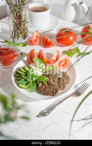 Raw cutlet made from vegetables and cereals with vegetables and herbs on a white plate with hard light Stock Photo