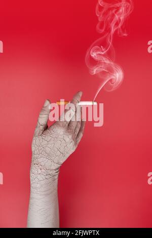 Dry and cracked hand holding a smoking cigarette. Bad effects of smoking on skin. Creative concept. Stock Photo
