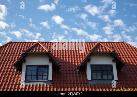 Red tiled roof with two dormers in front of a blue sky with clouds Stock Photo