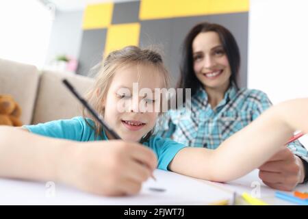 Little girl draws with pencils on background sitting woman Stock Photo