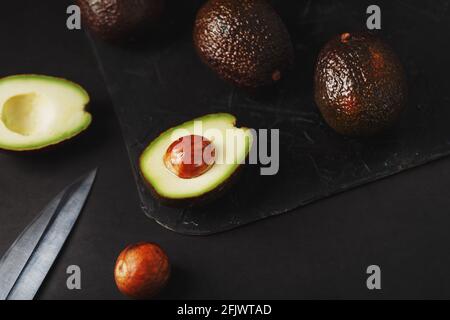 Sliced and whole organic avocado Hass with a knife on a black background. A source of essential fats, vitamins, trace elements, beta-carotene and omeg Stock Photo
