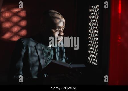 African priest reading the Bible while sitting in the confessional Stock Photo