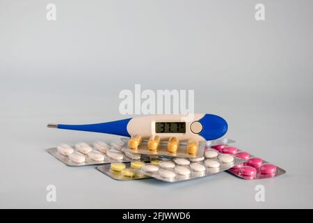Different medicines - tablets and pills in blister pack, medications drugs and electronic thermometer shows elevated temperature - sign of illness. Stock Photo