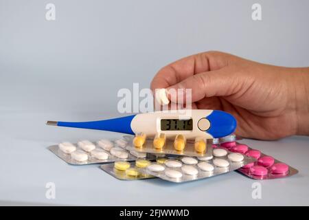 Different medicines- tablets and pills in blister pack, medications drugs, electronic thermometer and woman's hand with pill. Stock Photo