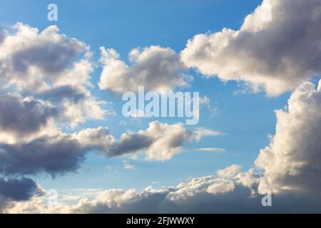 The blue sky shines through the gray diverging clouds under the pressure of the sun's rays. Stock Photo