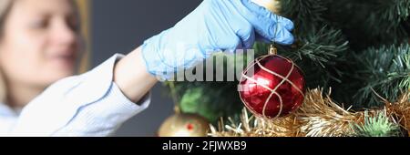 Woman in protective rubber gloves hanging ball on Christmas tree closeup Stock Photo