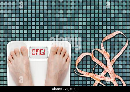 Woman on bathroom scale displaying OMG message. Concept of overweight, obesity or unhealthy lifestyle with measuring tape on bathroom floor. Stock Photo