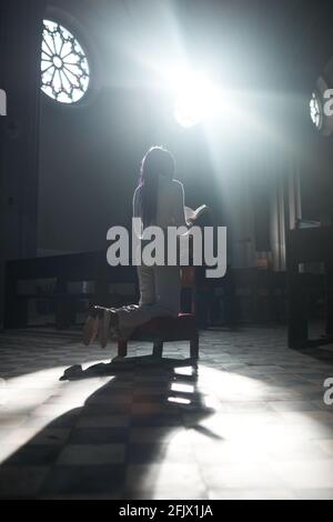 Rear view of woman reading the prayers sitting in chair in the church Stock Photo