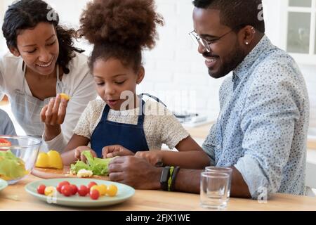 Happy family couple and daughter girl preparing salad in kitchen Stock Photo