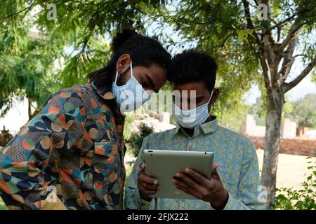 Portrait of two young Indian friends in a medical face mask using a digital tablet in the park Stock Photo