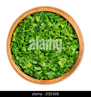 Chopped parsley, in a wooden bowl. Fresh, flat leaved parsley, green leaves of Petroselinum crispum, used as herb, spice and vegetable. Close-up. Stock Photo