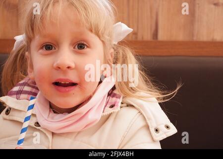 A little girl in a cafe drinks a drink from a striped tube Stock Photo