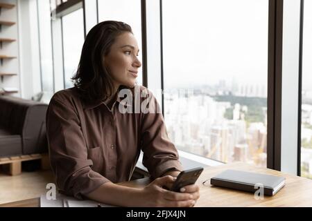 Young woman use smartphone look in distance dreaming Stock Photo