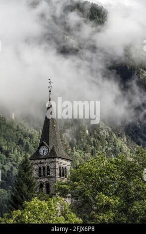 bell tower of a church with a big clock in a mountain village in the Pyrenees with clouds behind it coming down the mountainside, church of Arties, Ll Stock Photo