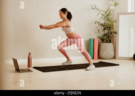 Woman doing lunges workout watching online class. Female in fitness wear teaching exercise to students online with her laptop. Stock Photo