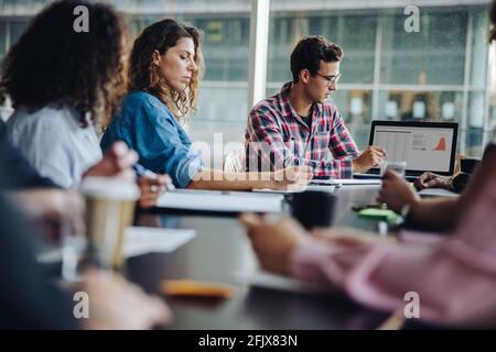 Group of businesspeople sitting in boardroom with laptop on table. Team of professionals having meeting. Stock Photo