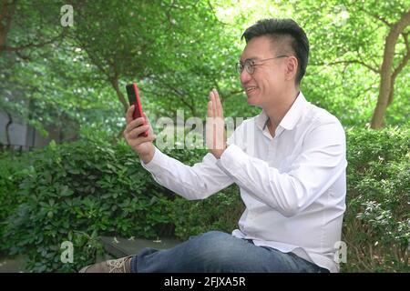 Asian businessman waving his hand, having video chat using his smartphone, outdoors. Stock Photo