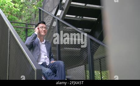 Businessman sitting on stairs with phone on his ear, chatting and smiling. Urban setting, copy space. Stock Photo