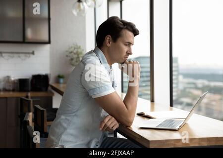 Pensive male employee work on laptop thinking Stock Photo