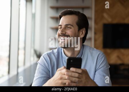 Smiling young man use cellphone looking in distance Stock Photo