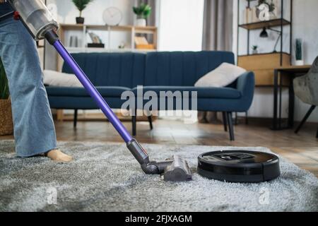 Close up of young woman cleaning carpet with hands vacuum cleaner while another wireless robot washing floor. Concept of technology and households. Stock Photo