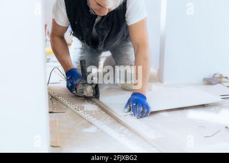 Close up tiler builder worker working with floor tile cutting equipment at repair renovation work. DIY, Do it yourself concept. House improvement Stock Photo