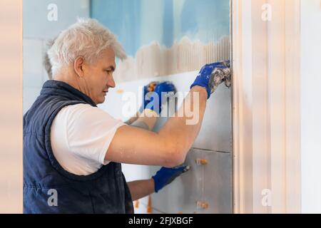 Two tilers installing wall tile at home. Father and son laying tiles on a bathroom wall. DIY, Do it yourself concept. House improvement. Repair Stock Photo