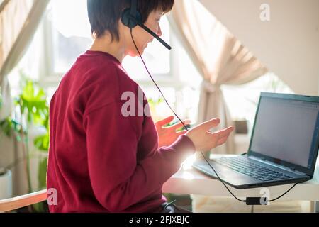 Woman in headset has video meeting or call. Customer service support representative working from home on a laptop. Freelance operator working in Stock Photo