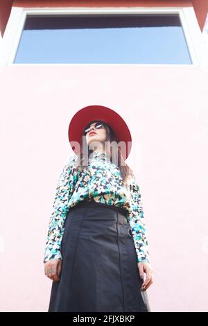 Stylish woman wearing a red hat standing on a light pink wall Stock Photo