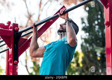 Dark-haired athlete with beard doing a pull-up on a calisthenics bar. Outdoor crossfit concept. Stock Photo