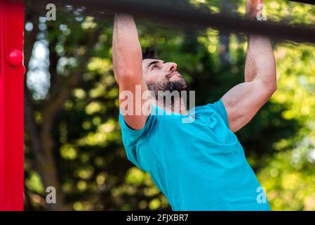 Dark-haired athlete with beard doing a pull-up on a calisthenics bar. Outdoor crossfit concept. Stock Photo