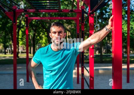 Portrait of Spanish brunette athlete after training. Red calisthenics bars in the background. Outdoor fitness concept. Stock Photo