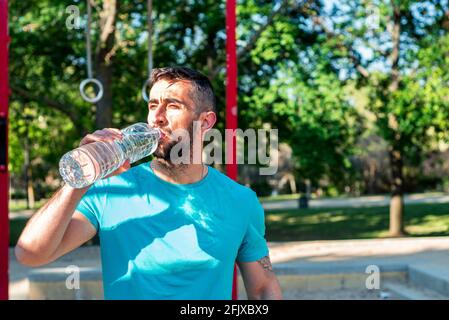 Bearded brunette man drinking water after workout in a park. Outdoor fitness concept. Stock Photo