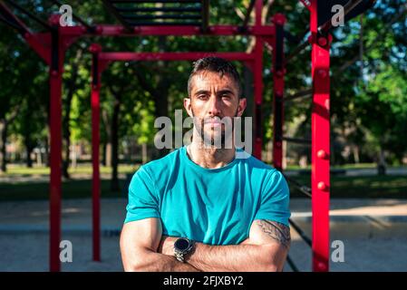 Portrait of Spanish brunette athlete after training. Red calisthenics bars in the background. Outdoor fitness concept. Stock Photo