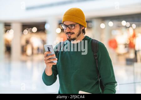 Modern spanish man smiling and using smartphone in shopping mall Stock Photo