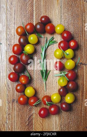 A sprig of rosemary on a wooden table surrounded by cherry tomatoes of different colors. Mediterranean food. Vegan and organic food Stock Photo