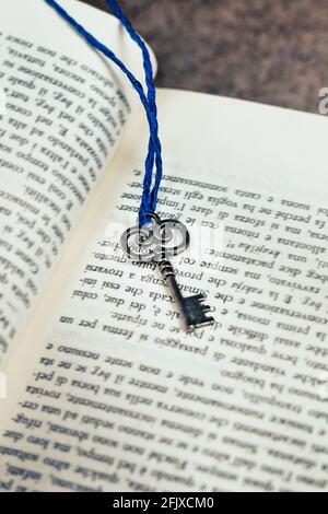 Silver key with blue string attached, placed on an open book Stock Photo