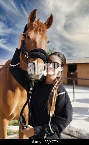 female horse racing jockey with her horse kissing, caressing and caring for him Stock Photo