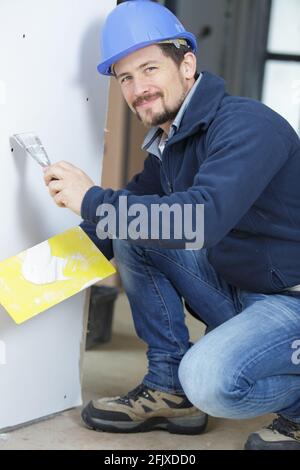 close up of smiling builder in hardhat sanding wall indoors Stock Photo