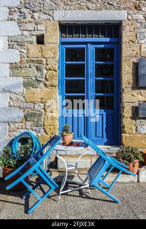Closed sidewalk cafe with chairs tilted onto small bistro table in front of brightly painted doors in old rock building Stock Photo