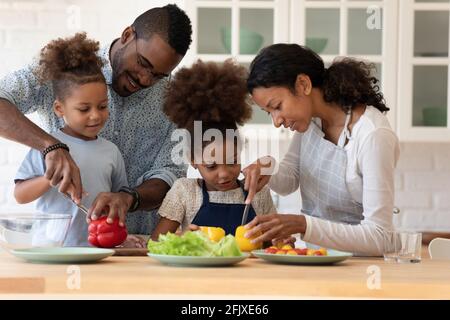 Happy family couple teaching two preschooler kids preparing salad Stock Photo