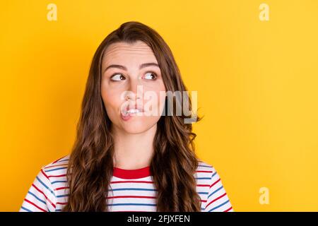 Photo of sweet doubtful young woman wear striped outfit biting lip looking empty space isolated yellow color background Stock Photo