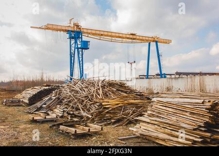 Industrial zone, construction site with piles of wooden waste and overhead hoist building crane. Stock Photo