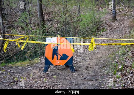 Construction sign with words 'trail closed' written on a piece of paper and attached to it. Yellow caution in tape surrounding sign. Trees background. Stock Photo