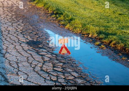 Yield sign reflected in a puddle of water on cracked asphalt. Writing backwards. Stock Photo